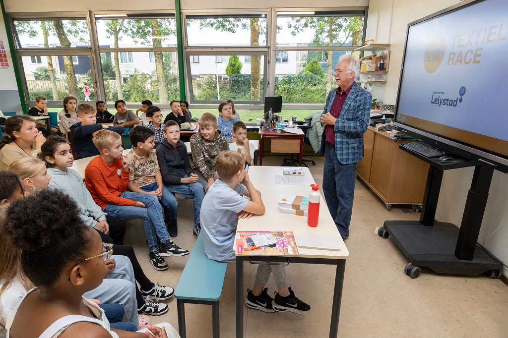 Wethouder Sjaak Kruis geeft in een klaslokaal het startsein voor de Textiel Race Lelystad